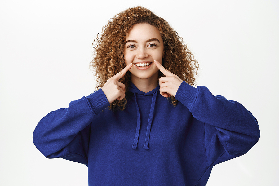 Dental Clinic Concept. Smiling Curly Girl In Blue Hoodie, Pointi